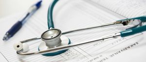 Ein Stethoskop liegt auf dem medizinischen Formular eines Patienten, mit einem Stift in der Nähe. Das Formular enthält Bereiche für Patientendaten und Gesundheitsaufzeichnungen.