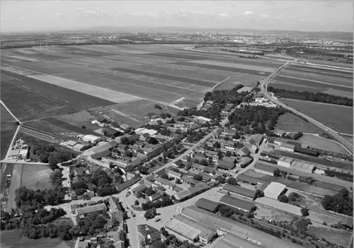 Eine Schwarz-Weiß-Luftaufnahme einer Stadt mit vielen Häusern und Gebäuden, umgeben von Feldern und Bäumen.