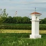 Ein weißer Turm mit einem braunen Dach steht in einem grasigen Feld mit Bäumen im Hintergrund und einem Silo in der Ferne.