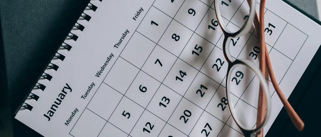 Ein weißer Kalender für Januar ist zu sehen. Ein Paar Brille liegt darauf. Er zeigt Wochentage und Daten an.