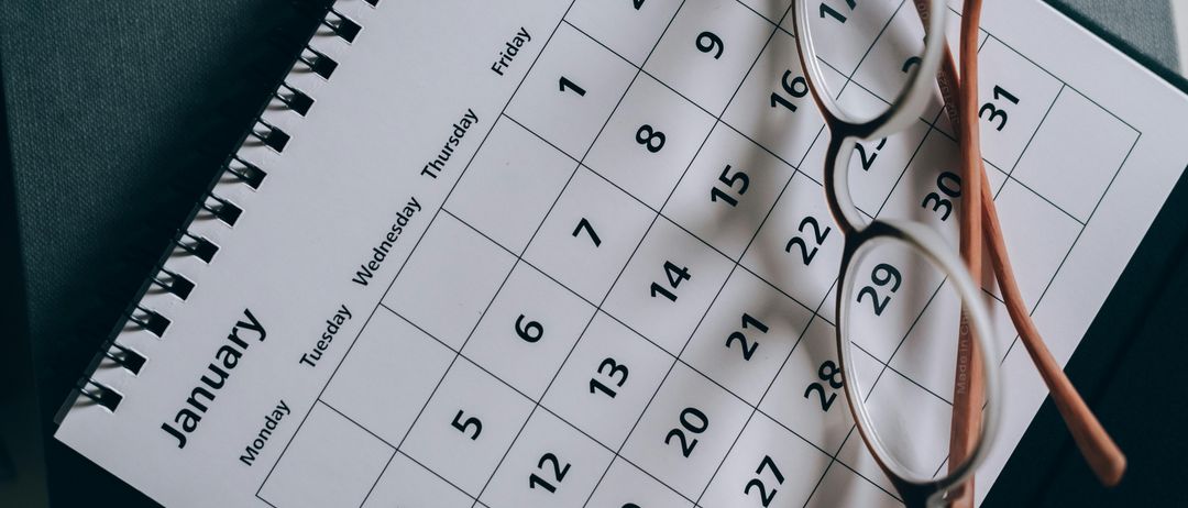 Ein weißer Kalender für Januar ist zu sehen. Ein Paar Brille liegt darauf. Er zeigt Wochentage und Daten an.