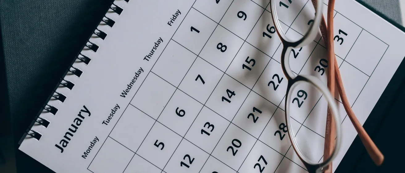 Ein weißer Kalender für Januar ist zu sehen. Ein Paar Brille liegt darauf. Er zeigt Wochentage und Daten an.
