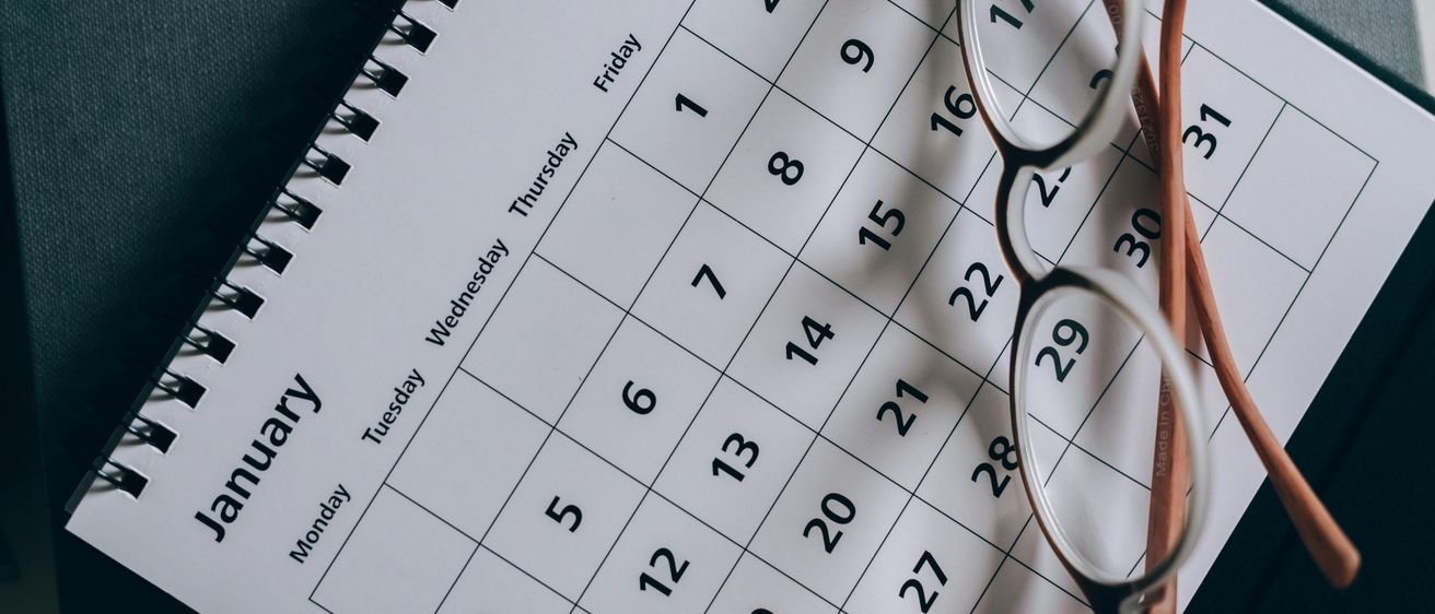 Ein weißer Kalender für Januar ist zu sehen. Ein Paar Brille liegt darauf. Er zeigt Wochentage und Daten an.