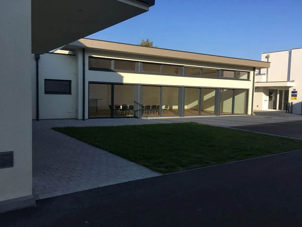 Ein modernes Gebäude mit großen Glasfenstern und einem großen Rasen davor. Das Gebäude hat eine Glasschiebetür und eine Nummer 6 an der Wand.