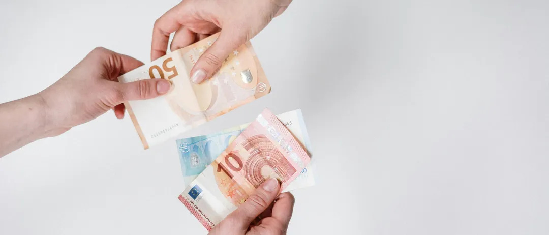 Zwei Hände tauschen zwei Euro-Banknoten aus, eine für eine 10-Euro-Banknote und eine für eine 5-Euro-Banknote. Die Banknoten liegen auf einem weißen Hintergrund.
