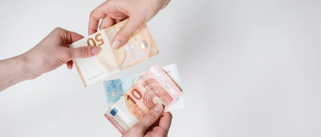 Zwei Hände tauschen zwei Euro-Banknoten aus, eine für eine 10-Euro-Banknote und eine für eine 5-Euro-Banknote. Die Banknoten liegen auf einem weißen Hintergrund.