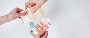 Zwei Hände tauschen zwei Euro-Banknoten aus, eine für eine 10-Euro-Banknote und eine für eine 5-Euro-Banknote. Die Banknoten liegen auf einem weißen Hintergrund.