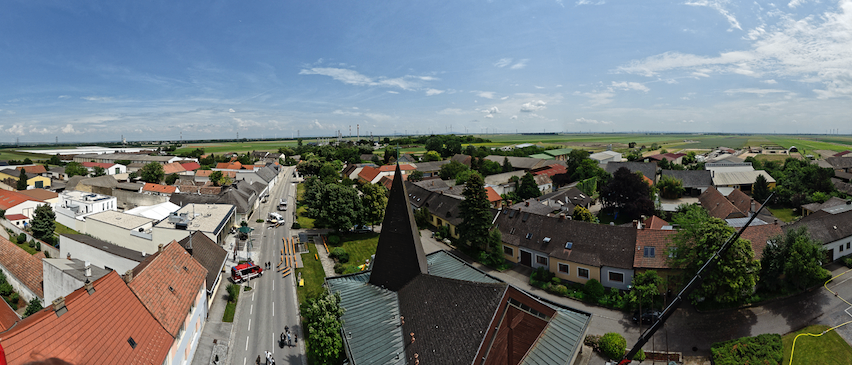 Ein Luftbild einer Stadt mit vielen Gebäuden, Bäumen und einer Straße. Ein Feuerwehrwagen ist geparkt. Ein Kran steht am Straßenrand.