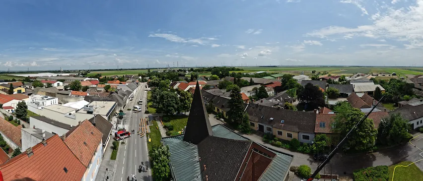Ein Luftbild einer Stadt mit vielen Gebäuden, Bäumen und einer Straße. Ein Feuerwehrwagen ist geparkt. Ein Kran steht am Straßenrand.