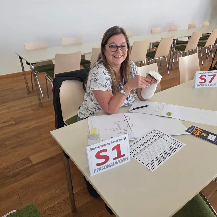 Eine Frau sitzt in einem Konferenzraum an einem Tisch, lächelt und hält eine verbundene Hand.