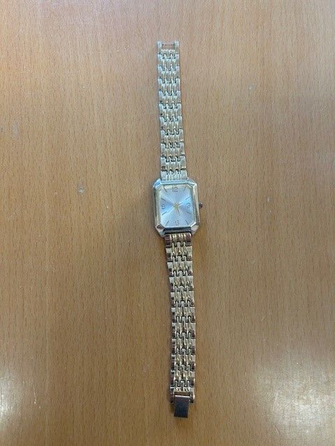Eine silberne Uhr mit quadratischem Zifferblatt, weißem Ziffernblatt und Metallkettenarmband auf einer Holzoberfläche.