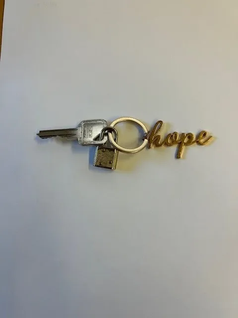 Ein Schlüsselanhänger mit dem Wort 'Hoffnung' in goldenen Buchstaben auf weißem Hintergrund.