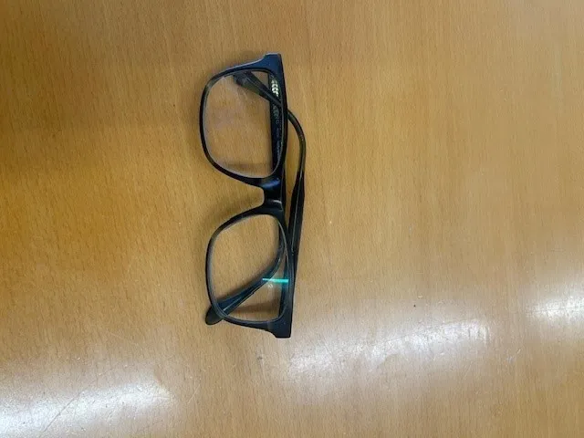 Ein Paar schwarzer Brille mit einem leichten grünen Schimmer auf einer Holzoberfläche.