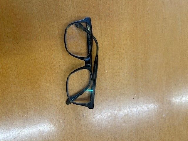 Ein Paar schwarzer Brille mit einem leichten grünen Schimmer auf einer Holzoberfläche.