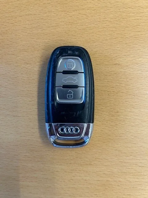 Ein schwarzer und silberner Audi-Autoschlüssel mit Logo und Tasten auf einer Holzoberfläche.