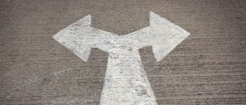 Ein weißes Richtungspfeilzeichen auf einer Betonoberfläche, das zwei mögliche Wege nach links und rechts anzeigt.