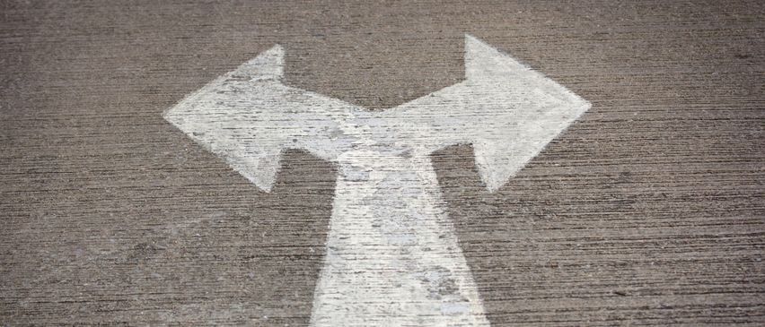 Ein weißer Pfeil, der auf einer Betonoberfläche nach oben zeigt. Der Pfeil besteht aus zwei sich schneidenden Linien.