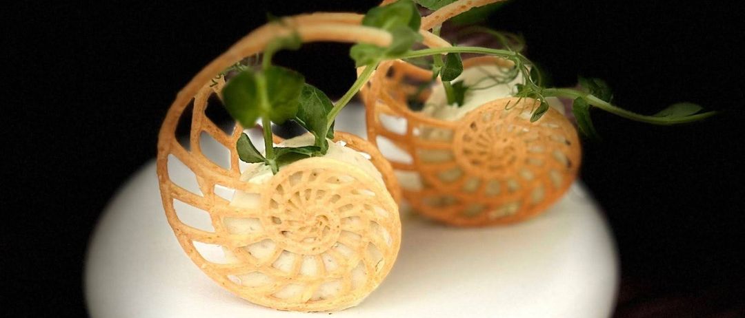 Zwei dekorative Gebäckspiralen mit Cremefüllung und grünen Blättern stehen auf einem weißen Teller auf einer Holzoberfläche.