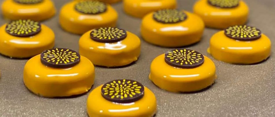 Mehrere gelbe Schokoladentrüffel mit einer schwarzen und gelben kreisförmigen Krönung liegen auf einem Backblech.