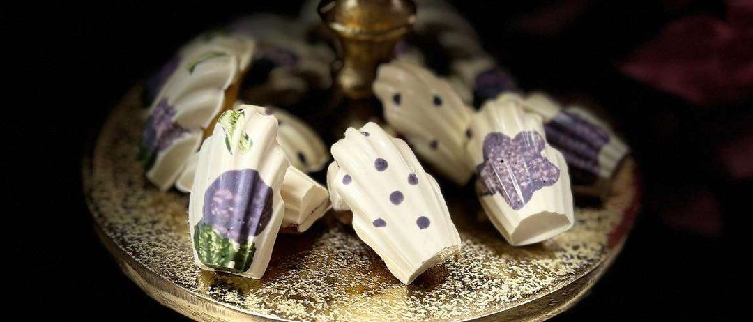 Eine Nahaufnahme von mehreren dekorativen weißen Schokoladenstücken mit violetten und grünen Designs auf einem goldenen Teller.