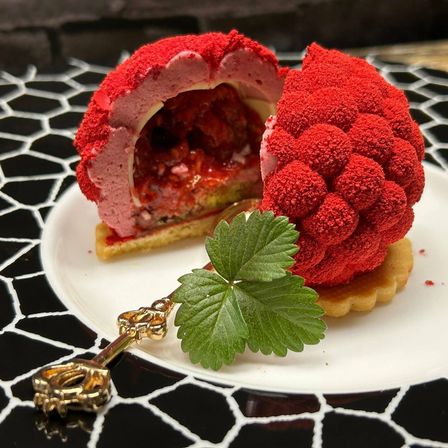 Ein Dessert mit roter Himbeerfüllung, einem Erdbeerblatt und einem goldenen Schlüssel auf einem gemusterten Teller.