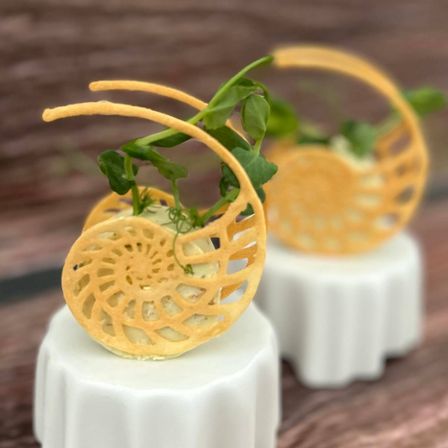 Zwei spiralförmige Desserts auf weißen Kuchenuntergründen stehen auf einem Holztisch. Die Desserts bestehen aus goldbraunen Waffeln und sind mit grünen Kräutern garniert.