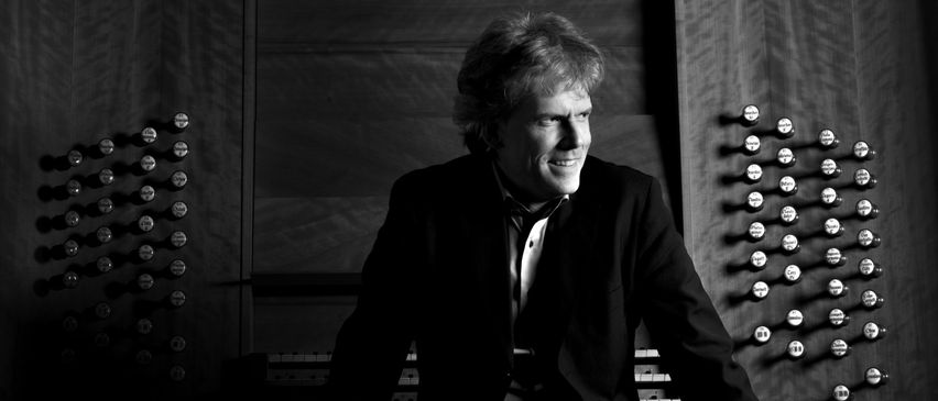 Ein Schwarz-Weiß-Foto eines Mannes in einem Anzug, der vor einer Orgel sitzt.