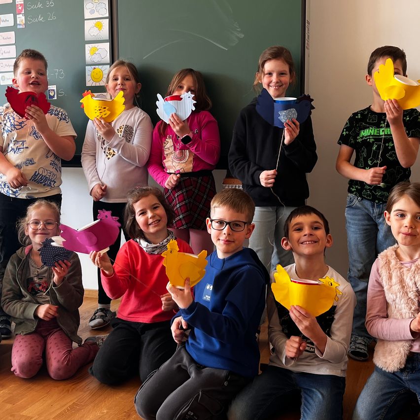 Ein Klassenzimmer voller Schüler, die Papierhühner vor einer Tafel halten.