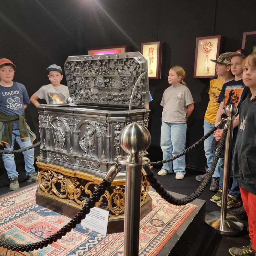 Mehrere Kinder betrachten einen verzierten, silbernen Sarg mit goldenen Akzenten, der in einem Museum ausgestellt ist.