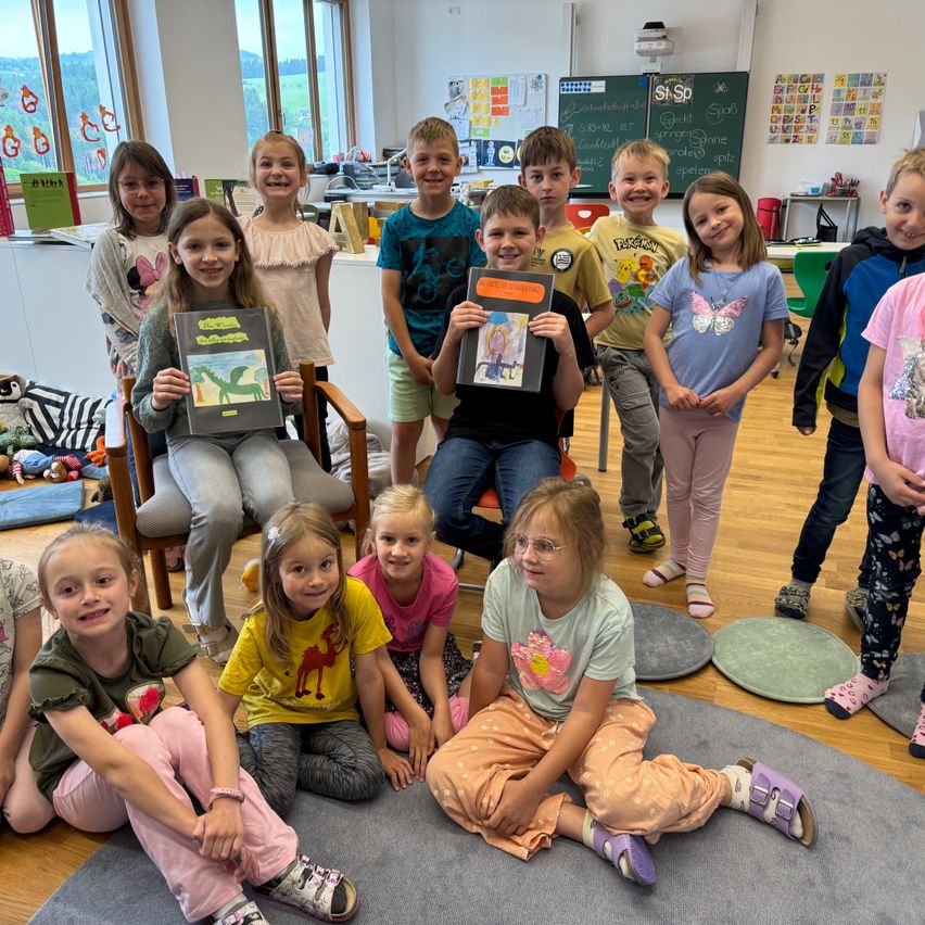 Eine Gruppe von Kindern in einem Klassenzimmer hält Bücher in den Händen. Sie sitzen und stehen und lächeln für ein Foto. Ein Mädchen mit Brille sitzt auf einem Stuhl und hält ein Buch.