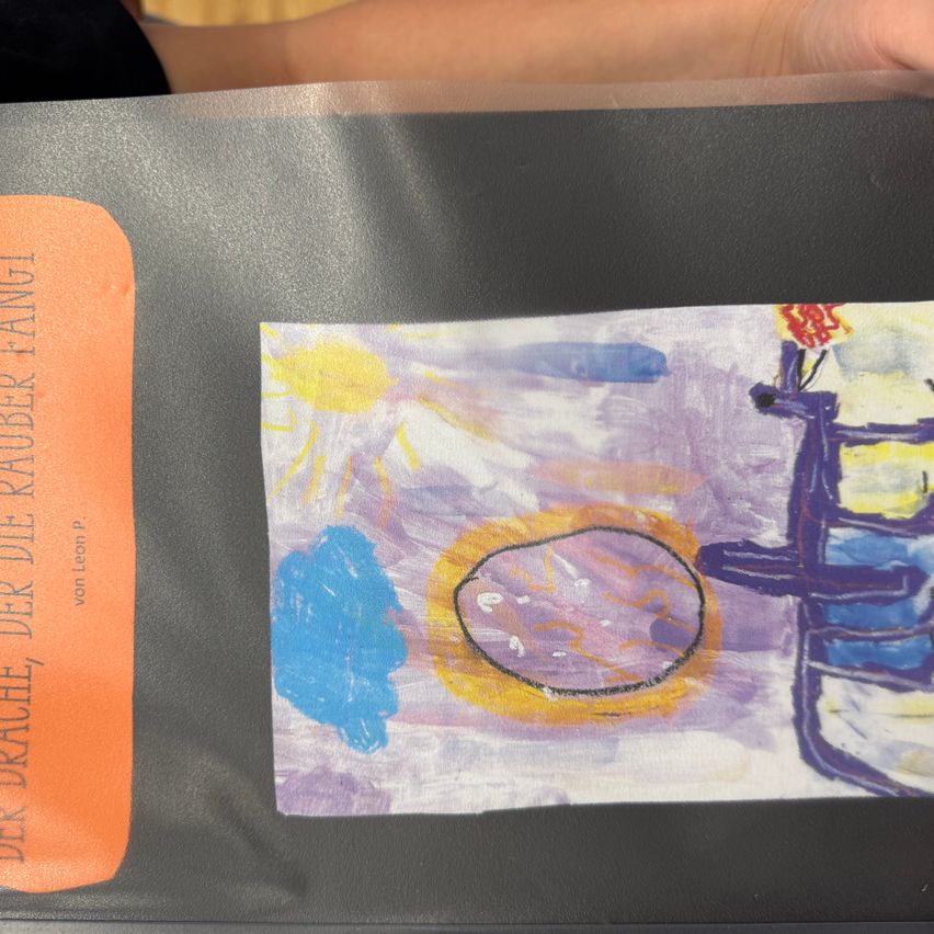 Ein Bild zeigt das Kunstwerk eines Kindes mit einer gelben Sonne, blauem Himmel und einer brückeartigen Struktur. Der Hintergrund ist lila und das Bild ist auf einer dunkelgrauen Oberfläche platziert.