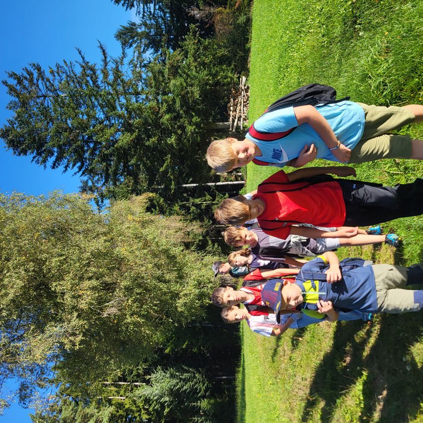 Eine Gruppe von Jungen liegt auf einem Grasfeld und posiert für ein Foto. Sie tragen Rucksäcke und Turnschuhe. Bäume und Sträucher umgeben das Gebiet.