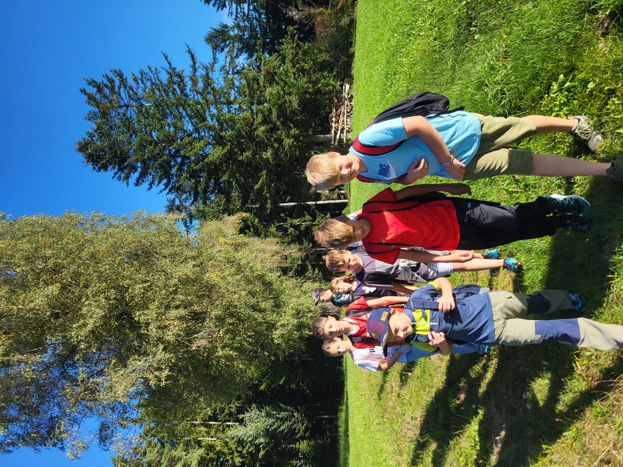 Eine Gruppe von Jungen liegt auf einem Grasfeld und posiert für ein Foto. Sie tragen Rucksäcke und Turnschuhe. Bäume und Sträucher umgeben das Gebiet.