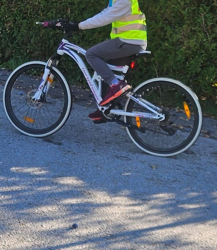 Ein junger Junge fährt auf einem Kiesweg mit dem Fahrrad. Er trägt einen Helm und eine reflektierende Weste.