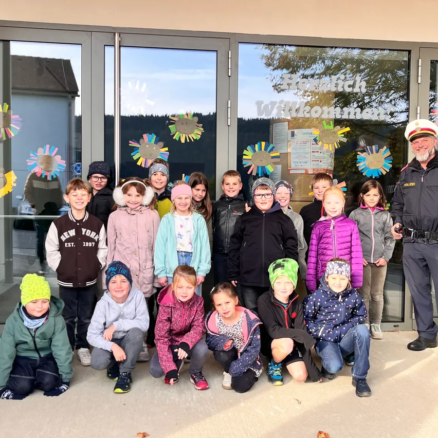 Eine Gruppe von Kindern und ein Polizeibeamter posieren für ein Foto vor einem Gebäude mit Glastüren.