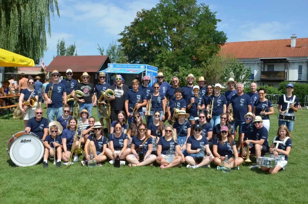 A group of musicians in blue shirts and hats pose for a photo on a grassy field with a food truck in the background.