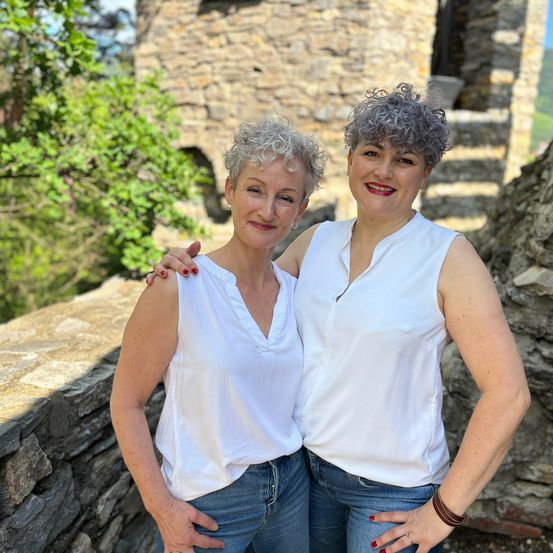 Zwei Frauen stehen nebeneinander vor einer Steinmauer.