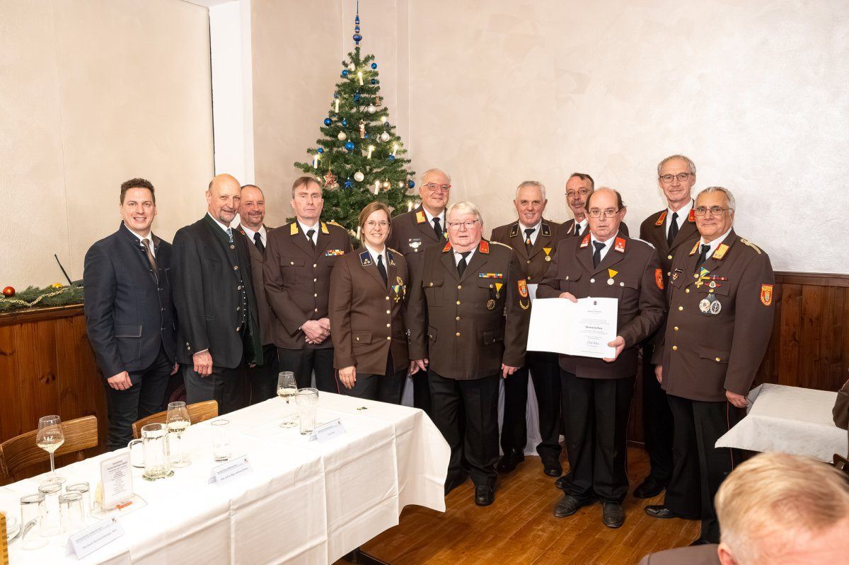 Eine Gruppe uniformierter Personen steht vor einem Weihnachtsbaum und Tisch und hält ein Zertifikat. Sie lächeln für ein Foto.