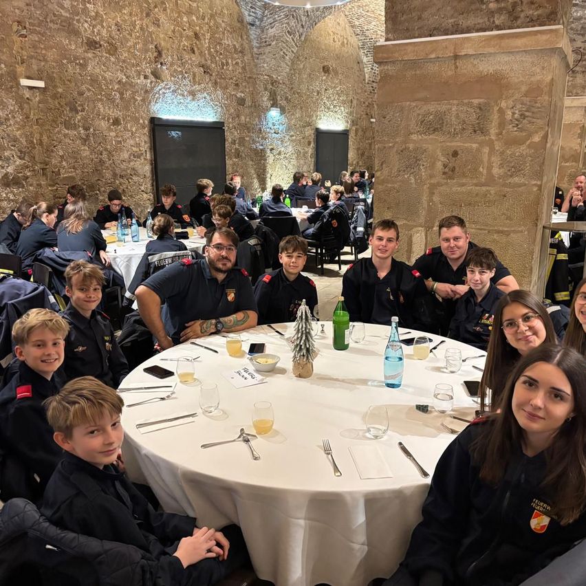 Eine Gruppe von Menschen, möglicherweise ein Team, versammelt sich in einem Raum mit Steinmauern. Sie lächeln und posieren für ein Foto an einem runden Tisch.