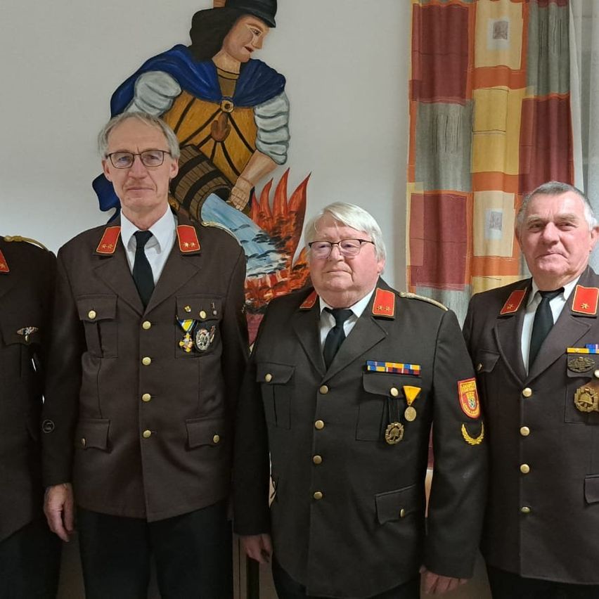 Vier Männer in Militäruniformen stehen nebeneinander, mit einer Wandmalerei eines Mannes in Rüstung hinter ihnen.