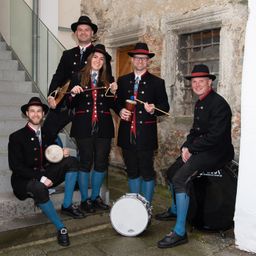 Eine Gruppe von Musikern in traditioneller Kleidung, posiert mit ihren Instrumenten vor einem alten Gebäude.