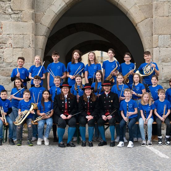 Eine Schulmusikband posiert mit ihren Instrumenten vor einem Bogen für ein Gruppenfoto.