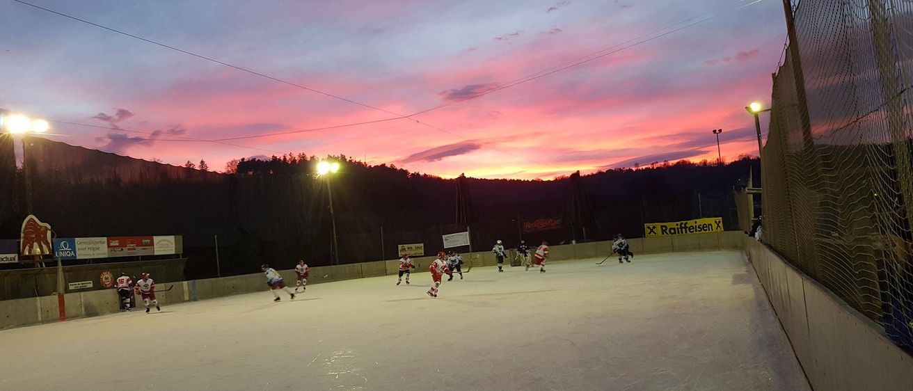 Eine Gruppe von Hockeyspielern skatet auf einer Freiluftbahn unter einem bunten Himmel. Straßenlaternen und Banner säumen die Bahn.