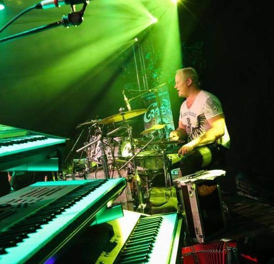 Ein Mann spielt die Drums auf einer Bühne, die von grünem Licht erhellt wird.