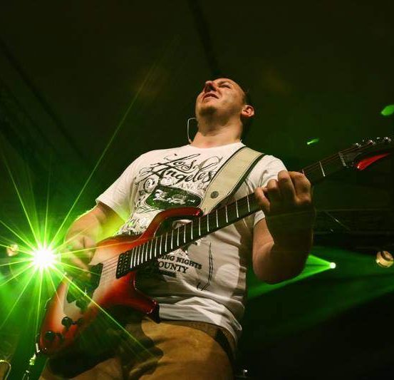 Ein Mann mit einer elektrischen Gitarre singt auf der Bühne, während grüne Lichter den Hintergrund beleuchten.