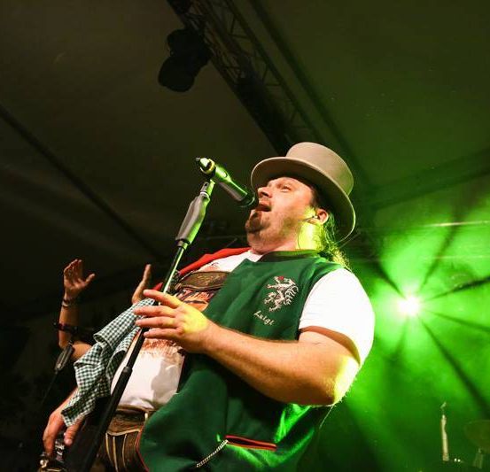 Ein Mann singt in ein Mikrofon, während ein anderer Gitarre spielt unter grünen Bühnenlichtern.