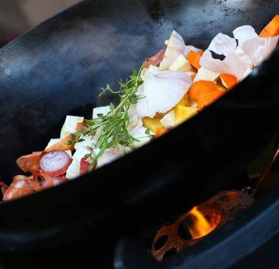 Ein Wok mit gehackten Gemüse und Kräutern kocht auf einem Herd mit Feuer.