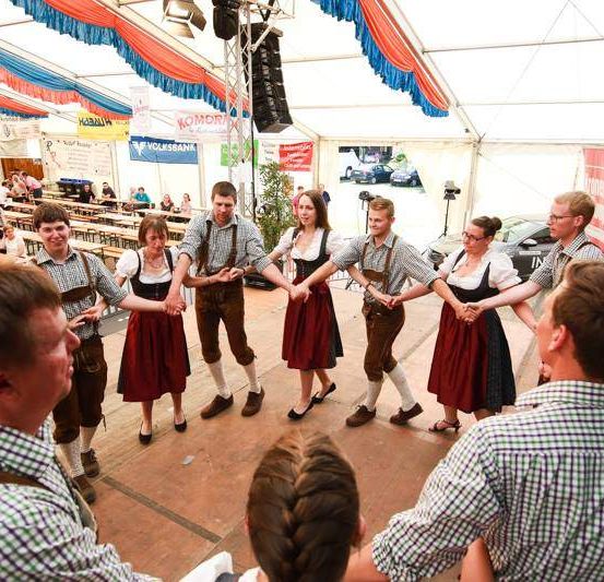 Eine Gruppe von Menschen führt einen traditionellen Tanz in einem festlichen Ambiente mit vielen Zuschauern auf.