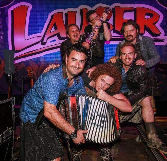 Fünf Personen lächeln und posieren für ein Foto auf der Bühne. Sie haben Musikinstrumente.