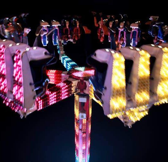 Ein bunter Fahrplatz mit Passagieren darin ist nachts beleuchtet und zeigt leuchtende rote und gelbe Lichter.